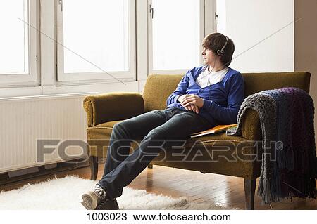 Stock Image - A teenage boy wearing headphones sitting on a couch. Fotosearch