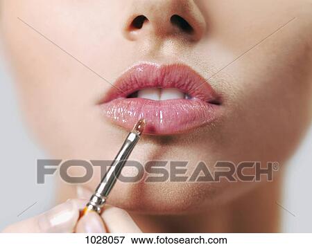 Stock Photo - A woman applying lip gloss with a make-up brush, close-up of lips. Fotosearch