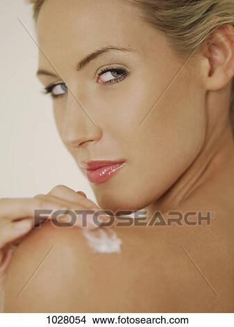 A woman applying moisturizer to her shoulder and looking over her shoulder View Large Photo Image Picture - A woman applying moisturizer to her shoulder and looking over her shoulder. Fotosearch