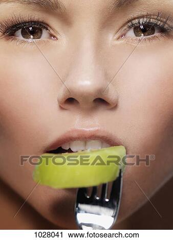A woman biting a slice of kiwi on a fork, close-up of face View Large Photo Image Stock Image - A woman biting a slice of kiwi on a fork, close-up of face. Fotosearch
