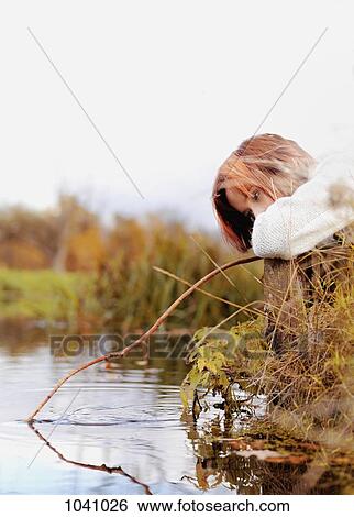 Stock Photograph - A woman dipping a stick in a stream . Fotosearch