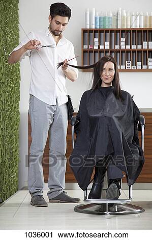 Stock Image - A woman having her hair cut by a male hairdresser . Fotosearch