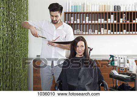 Stock Image - A woman having her hair cut by a male hairdresser. Fotosearch