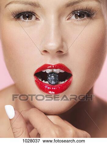 Stock Photo - A woman holding a blueberry between her teeth, close-up. Fotosearch
