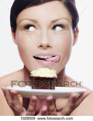 A woman holding a cupcake on a plate and licking her lips View Large Photo Image Stock Photo - A woman holding a cupcake on a plate and licking her lips. Fotosearch