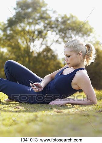 A woman in sports clothing sitting in grass reading a text message View Large Photo Image Stock Image - A woman in sports clothing sitting in grass reading a text message. Fotosearch