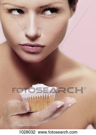 Stock Image - A woman looking to the side suspiciously while holding a cupcake. Fotosearch