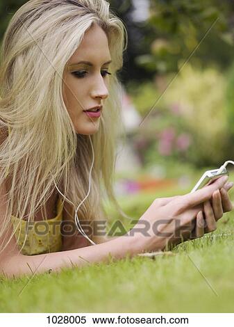 Stock Photography - A woman lying in the grass listening to an MP3 player. Fotosearch