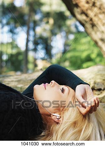 A woman lying outdoors wearing earphones, close-up, head and shoulders View Large Photo Image Stock Image - A woman lying outdoors wearing earphones, close-up, head and shoulders. Fotosearch