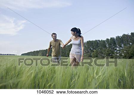 Stock Image - A woman pulling her boyfriend through a field. Fotosearch