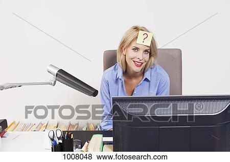 Stock Photo - A woman sitting at an office desk with an adhesive note on her forehead. Fotosearch