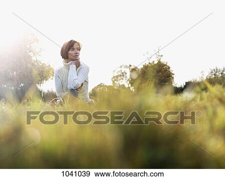 A woman sitting in the grass, looking away, low angle view View Large Photo Image Stock Photo - A woman sitting in the grass, looking away, low angle view. Fotosearch