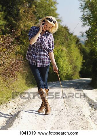 A woman walking down a remote dirt road using a mobile phone View Large Photo Image Stock Photo - A woman walking down a remote dirt road using a mobile phone. Fotosearch
