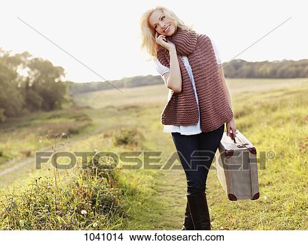 A woman walking in the country carrying a suitcase while using a mobile phone View Large Photo Image Picture - A woman walking in the country carrying a suitcase while using a mobile phone. Fotosearch