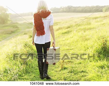 A woman walking in the country carrying a suitcase View Large Photo Image Stock Photo - A woman walking in the country carrying a suitcase. Fotosearch