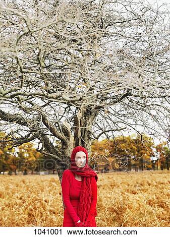 A woman wearing a bright red dress and scarf standing under a leafless tree in nature View Large Photo Image Stock Image - A woman wearing a bright red dress and scarf standing under a leafless tree in nature. Fotosearch