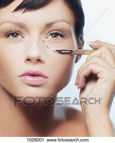 A woman with a dotted line under her eye holding a scalpel View Large Photo Image Stock Image - A woman with a dotted line under her eye holding a scalpel. Fotosearch