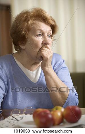 A worried senior woman sitting at a table with her hand covering her mouth View Large Photo Image Stock Image - A worried senior woman sitting at a table with her hand covering her mouth . Fotosearch