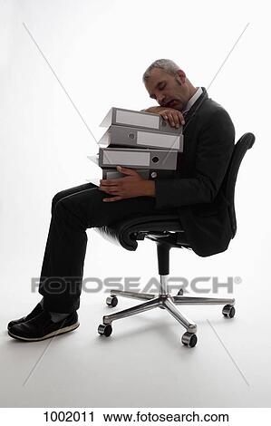 Stock Image - An exhausted businessman resting his head on a stack of binders. Fotosearch