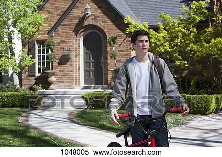 Stock Photography - Boy standing still holding bike outside his house. Fotosearch