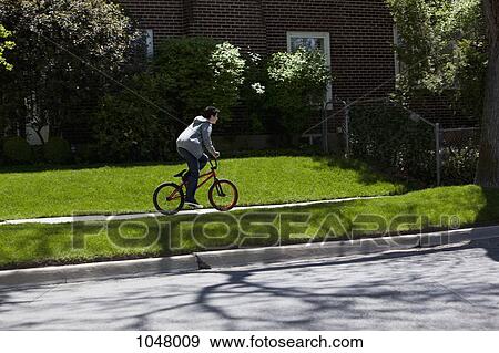 Boy stands while riding bike on footpath View Large Photo Image Stock Photo - Boy stands while riding bike on footpath. Fotosearch