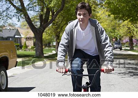Stock Photo - Boy stands while riding bike with a content facial expression. Fotosearch