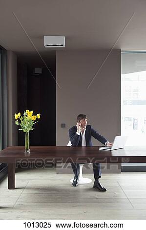 Stock Photography - Businessman at home on phone using laptop.. Fotosearch