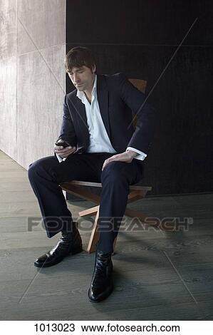 Stock Image - Businessman sits with phone in hand texting a message. . Fotosearch