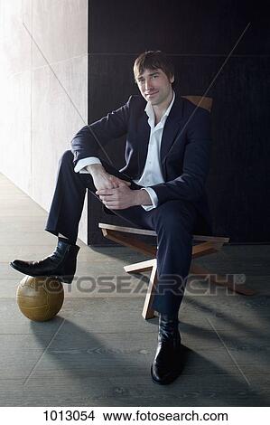 Businessman sitting with foot on soccer ball and looking at camera. View Large Photo Image Picture - Businessman sitting with foot on soccer ball and looking at camera.. Fotosearch
