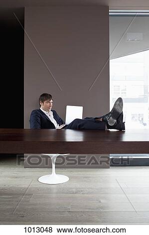 Stock Photo - Businessman with feet up on table using laptop.. Fotosearch