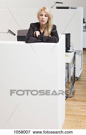 Stock Photo - Businesswoman leaning on office cubicle looking down. Fotosearch