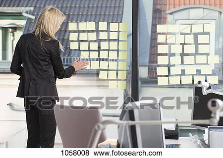 Stock Photo - Businesswoman sticking many reminder notes to her office window. Fotosearch