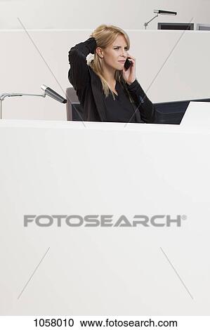 Businesswoman with hand on head talking on phone at office cubicle View Large Photo Image Stock Image - Businesswoman with hand on head talking on phone at office cubicle. Fotosearch