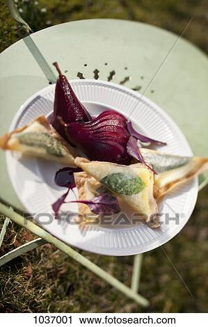 Stock Image - Cheese toast triangles and sliced pickled pears on a paper plate, on a chair outside . Fotosearch
