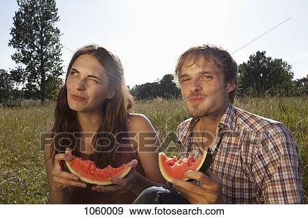 Stock Photo - Couple sitting eating melon in field. Fotosearch