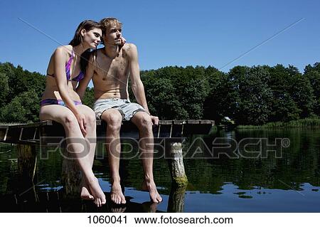 Couple sitting on edge of jetty by lake View Large Photo Image Stock Image - Couple sitting on edge of jetty by lake. Fotosearch