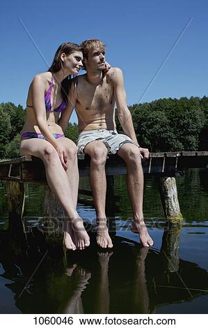 Couple sitting on edge of jetty by lake View Large Photo Image Stock Photograph - Couple sitting on edge of jetty by lake. Fotosearch