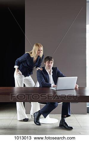 Stock Image - Couple work from home enjoying looking at laptop.. Fotosearch