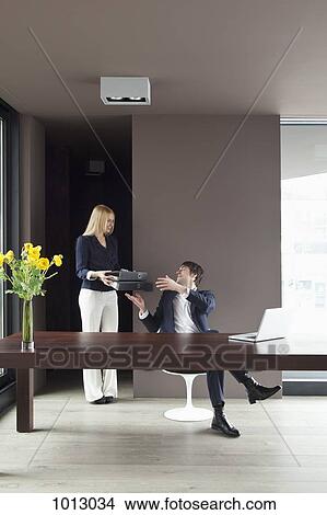 Picture - Couple work from home. Woman hands over files.. Fotosearch