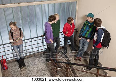 Stock Image - Five teenage boys talking and ignoring a teenage girl in a school stairwell. Fotosearch