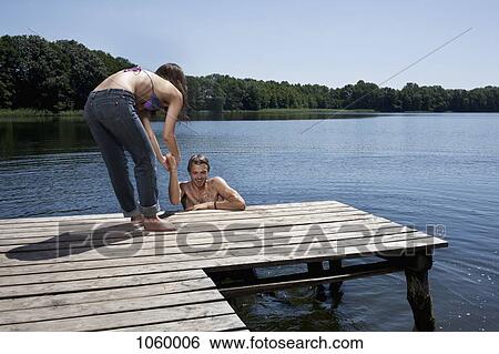 Fun as woman helps man out of the water on jetty View Large Photo Image Stock Photograph - Fun as woman helps man out of the water on jetty. Fotosearch