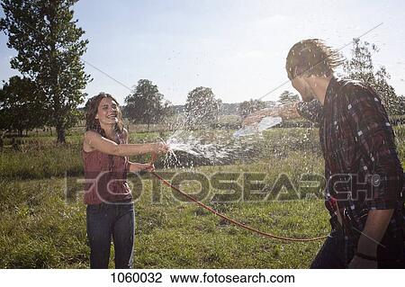 Girl sprays guy with hose in a field View Large Photo Image Stock Image - Girl sprays guy with hose in a field. Fotosearch