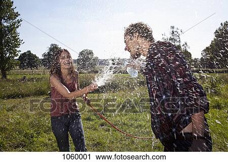 Stock Image - Girl sprays guy with hose on field. Fotosearch