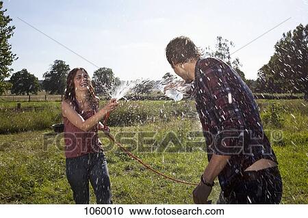 Stock Image - Girl sprays guy with hose on field. Fotosearch