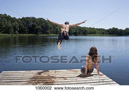 Guy dives into lake with arms outstretched as girl watches on jetty View Large Photo Image Stock Image - Guy dives into lake with arms outstretched as girl watches on jetty. Fotosearch