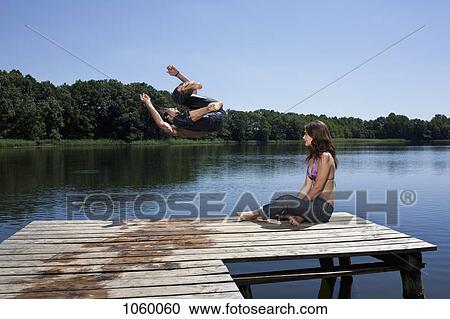 Guy jumps into lake with arms outstretched as girl watches on jetty View Large Photo Image Stock Image - Guy jumps into lake with arms outstretched as girl watches on jetty. Fotosearch