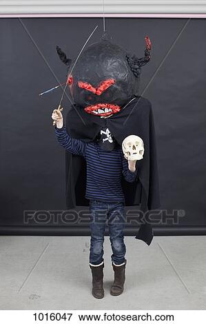 Stock Photo - Kid with Halloween outfit on, a skull in his hand and a toy sword. Fotosearch