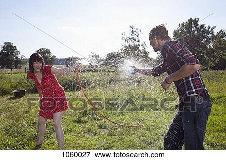 Stock Photo - Man and woman spray each other with water in field. Fotosearch