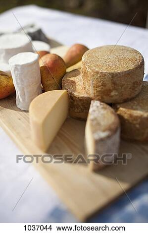 Picture - Pears and a variety of cheese on a chopping board on a table outside. Fotosearch