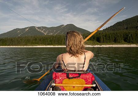 Rear view of woman paddling a canoe with mountain range in background View Large Photo Image Stock Photo - Rear view of woman paddling a canoe with mountain range in background. Fotosearch